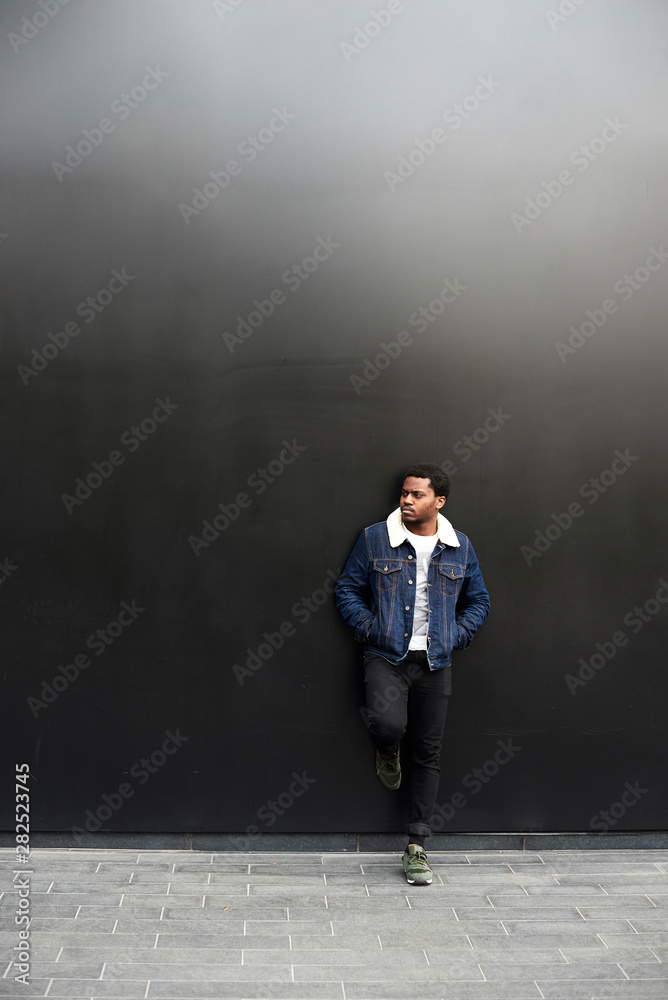 Man wearing denim jacket standing in front of dark background Man wearing denim jacket standing in front of dark background