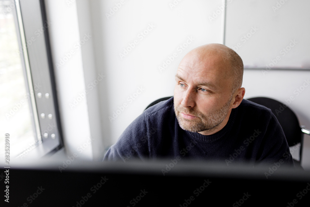 Pensive man sitting in front of a computer and looking out of the window Pensive man sitting in front of a computer and looking out of the window