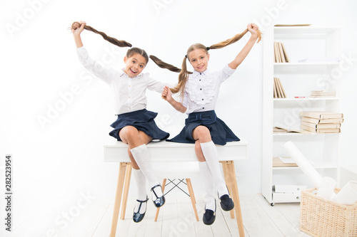 Successful team. Little schoolgirls classmates kids. Schoolgirls friends sit on desk. Best friends relaxing. Schoolgirls tidy hairstyle relaxing having rest. School uniform. Rebellious spirit photo