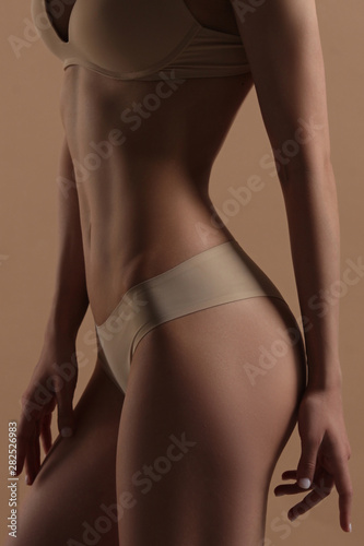 Thin young woman in underwear on beige background