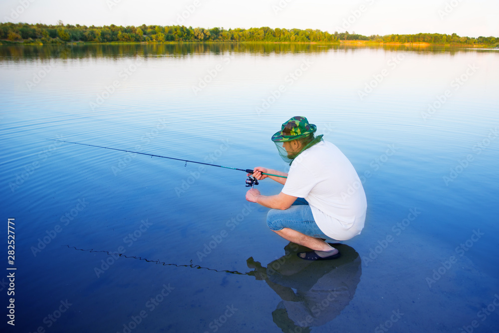 man catches a fish spinning on the background of water in the summer. Russian fishing man catches a fish spinning on the background of water in the summer. Russian fishing
