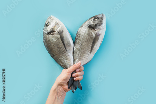 Photography Female hand with two dorado fish tail on blue paper as color of sea