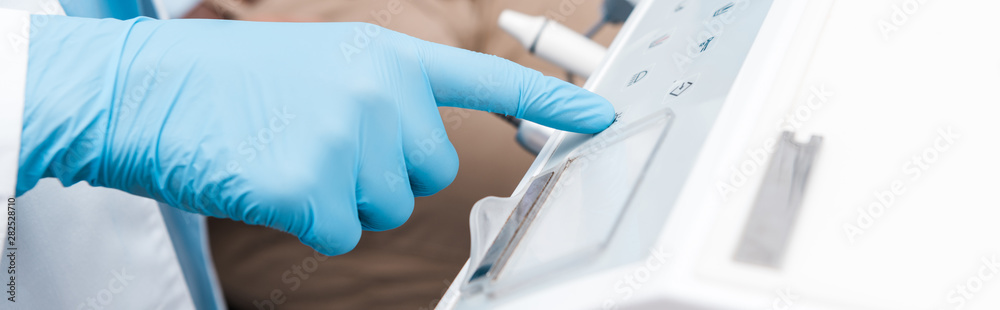 panoramic shot of dentist in blue latex glove pointing with finger at dental equipment