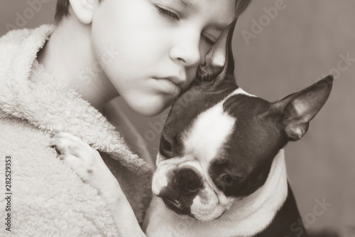 The boy cares, loves and tenderly embraces his devoted friend the Boston Terrier dog. Black and white photo. © leksann