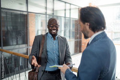 Cheerful dark-skinned man smiling while talking to business partner