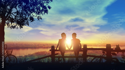 Boy and girl hold hands looking at setting sun after a bike ride