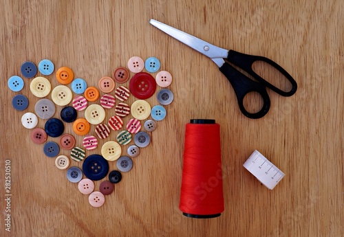 Botões em formato de coração, tesoura, linha de costura e fita métrica. Conceito de costura com plano de fundo de madeira. photo