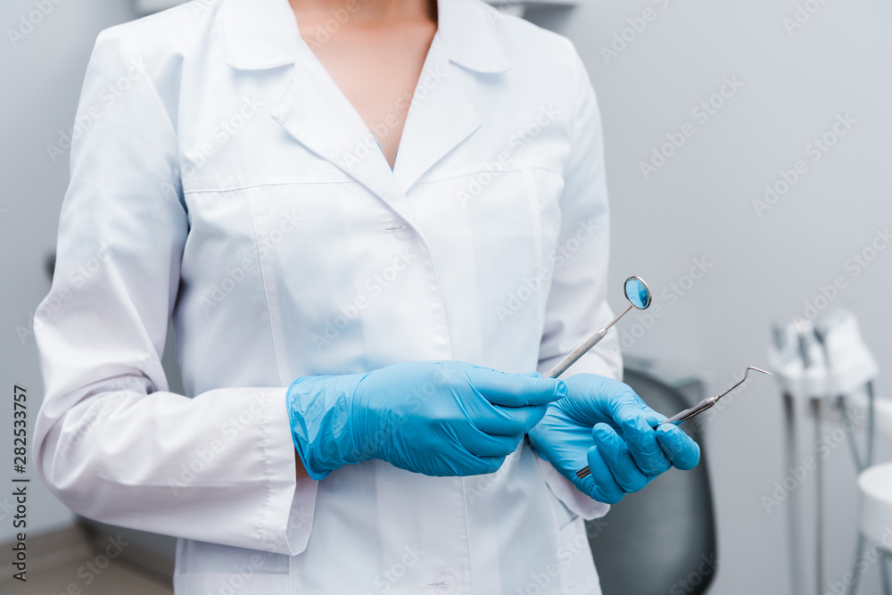 cropped view of dentist in blue latex gloves holding stainless medical instruments