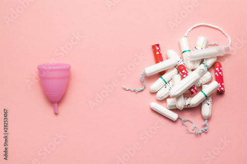 Reusable silicone menstrual cup and heap of tampons comparison on a soft pink background. Modern female intimate alternative gynecological hygiene. Eco zero waste concept