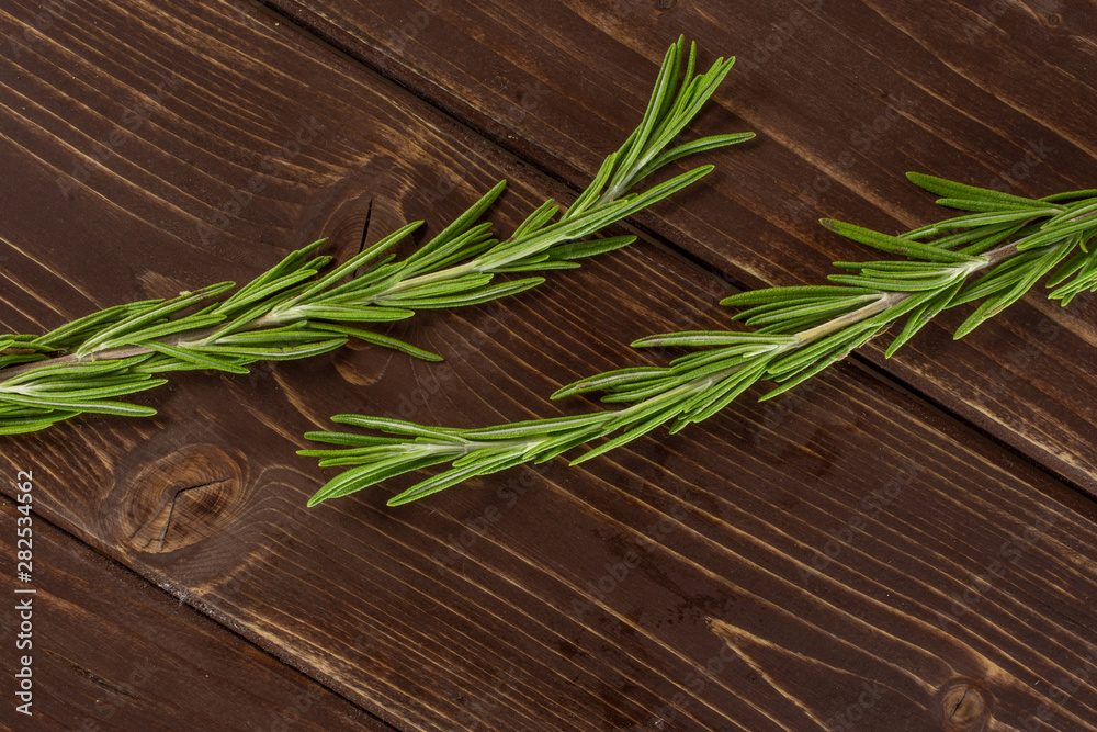 Group of two whole fresh evergreen sprig of rosemary flatlay on brown wood