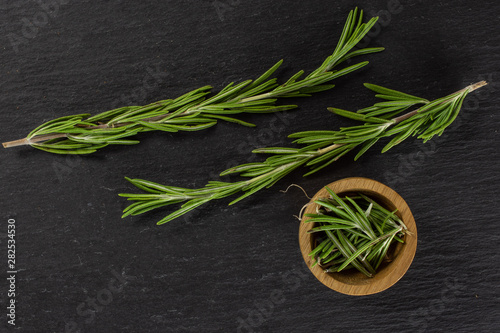 Group of two whole lot of pieces of fresh evergreen sprig of rosemary in a wooden bowl flatlay on grey stone
