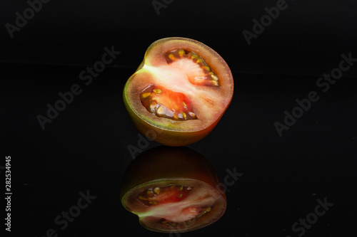 One half of fresh greenish red tomato isolated on black glass