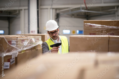 Warehouse worker scanning boxes with bar code reader in warehouse distribution center. Sorting out and shipping packages to destination. photo