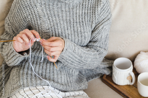 girl in a warm gray sweater knits sitting on a sofa in a cozy interior hygge