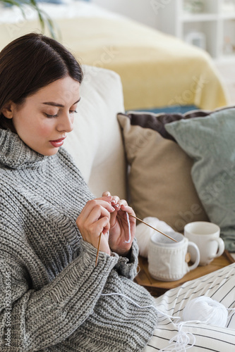 girl in a warm gray sweater knits sitting on a sofa in a cozy interior hygge