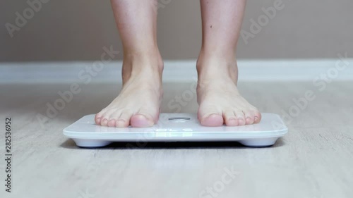 Daily weight measurement, female legs stand on digital smart scales in close-up