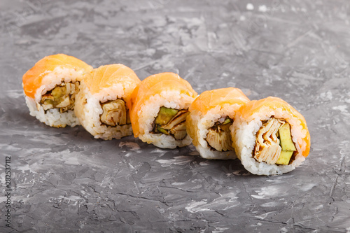 Japanese maki sushi rolls with salmon, avocado and omelette on black concrete background. Side view.