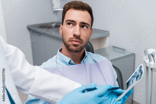 cropped view of dentist holding x-ray near handsome patient