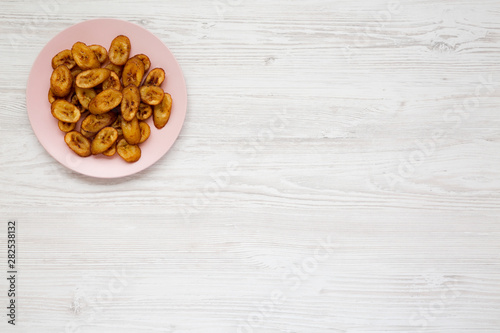 Homemade fried plantains on a pink plate over white wooden background, view from above. Flat lay, overhead, from above. Copy space.