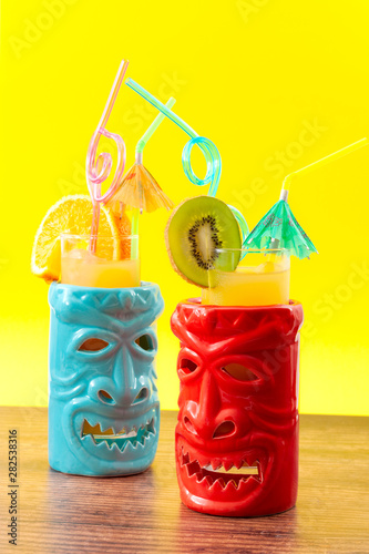 Obraz na płótnie Hawaiian tiki bar, summer refreshing drinks and tropical cocktails concept theme with glasses of alcohol and juice mixed together, kiwi and orange slices, umbrella and drinking straw on wooden table w salonie
