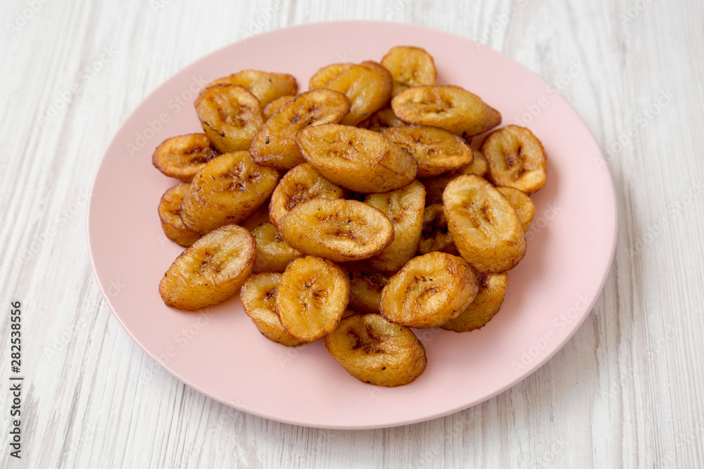 Homemade fried plantains on a pink plate on a white wooden surface, low angle view. Close-up.