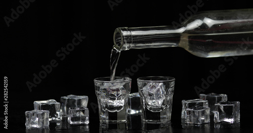 Pouring up shots of vodka from a bottle into glass. Black background