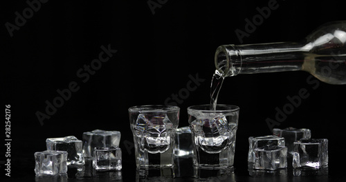 Pouring up shots of vodka from a bottle into glass. Black background