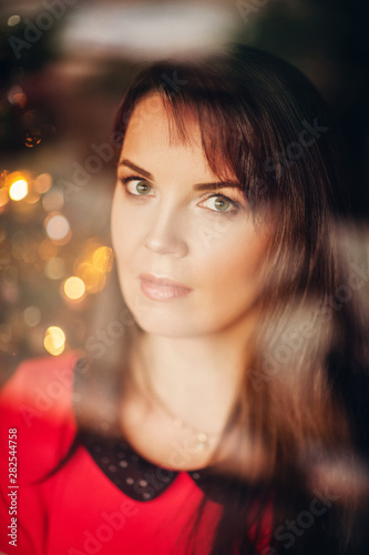Christmas portrait of beautiful woman with dark hair, wearing red dress, image taken through the window