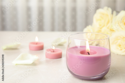 Burning candle in glass holder and roses on light table, space for text