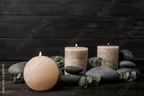 Composition with burning candles, spa stones and eucalyptus on dark wooden table