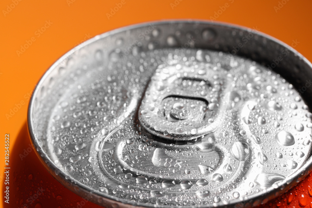 Aluminum can of beverage covered with water drops on orange background, closeup