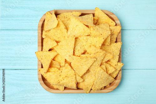 Wooden plate of tasty Mexican nachos chips on light blue wooden background, top view