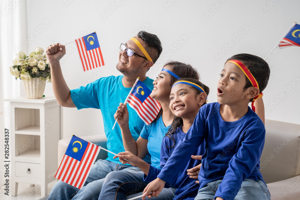 Obraz premium happy family with malaysia flag sitting on a couch watching soccer match