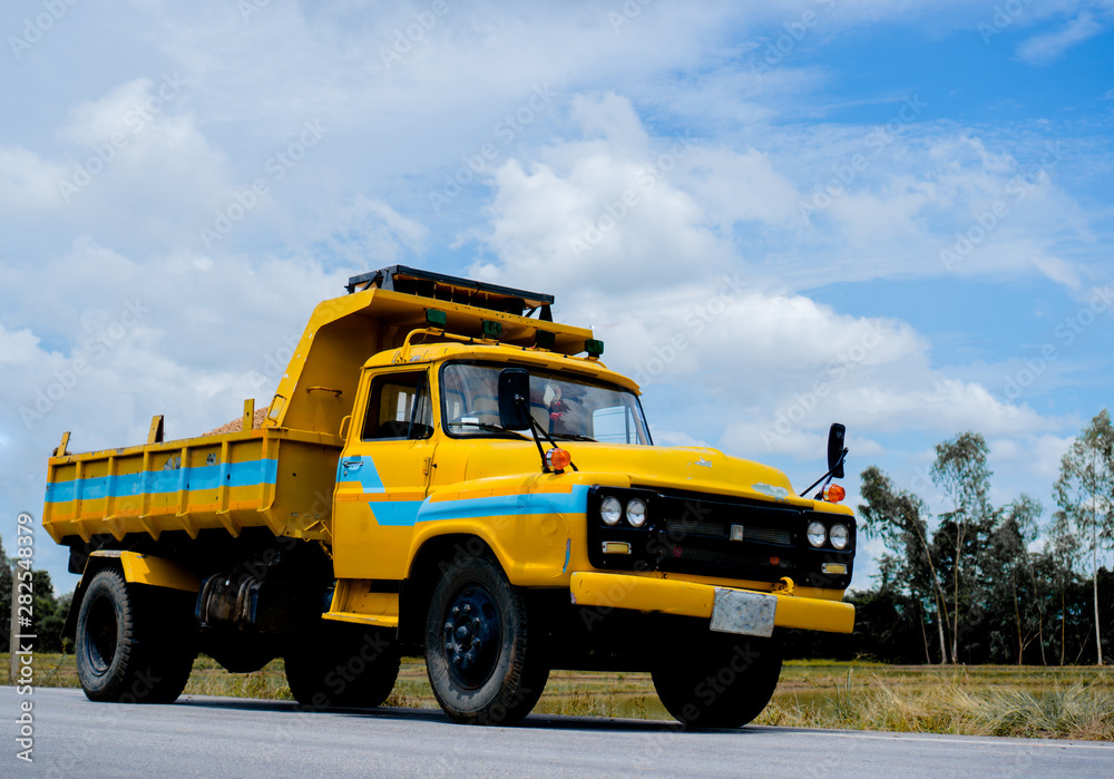 the yellow truck on the road with the beautiful sky and farm