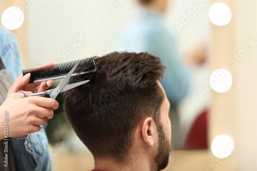 Foto Barber making stylish haircut with professional scissors in beauty salon, closeu
