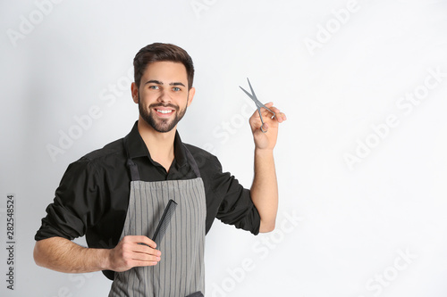Young hairstylist holding professional scissors and comb on light background