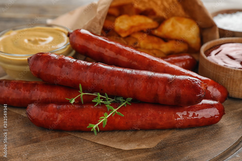 Delicious grilled sausages and sauces on wooden board, closeup. Barbecue food