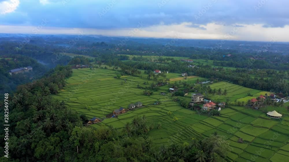 Aerial Forward: Buildings And Bright Green Fields In Vast Valley, Clouds Overhead - Jatiluwih Rice Terrace, Bali Aerial Forward: Buildings And Bright Green Fields In Vast Valley, Clouds Overhead - Jatiluwih Rice Terrace, Bali