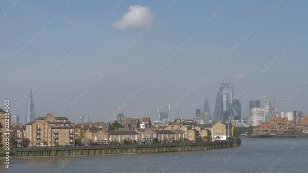 Residential flats on a riverside with financial buildings in the background.