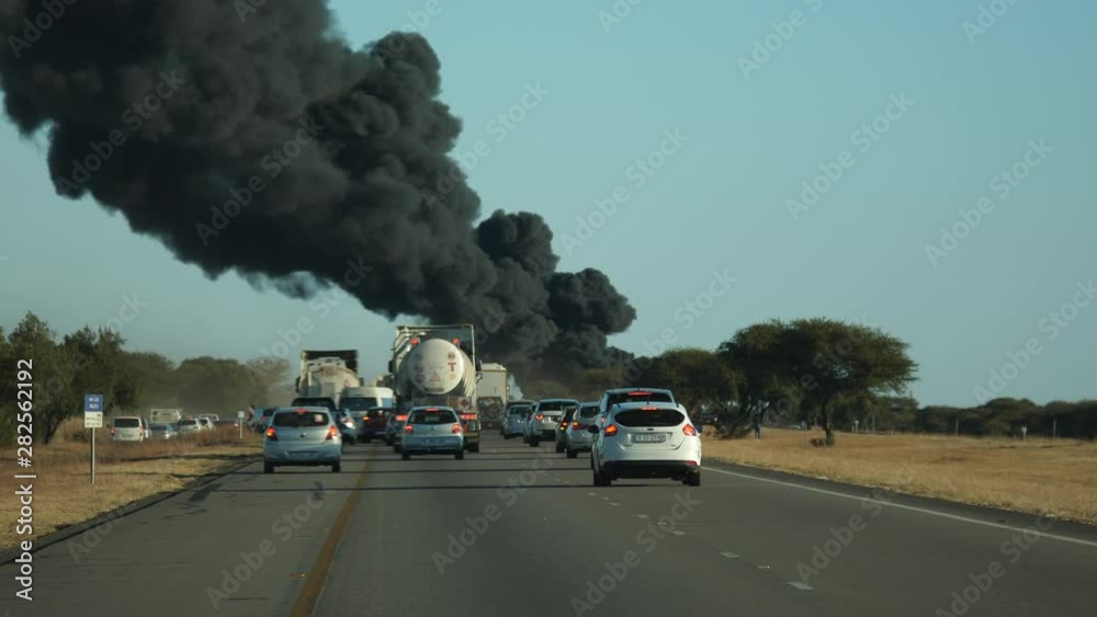 Traffic on highway comes to standstill as thick, black smoke and fireballs billow into the air from along the roadway. Cars and trucks in traffic jam, viewed from behind. Traffic on highway comes to standstill as thick, black smoke and fireballs billow into the air from along the roadway. Cars and trucks in traffic jam, viewed from behind.