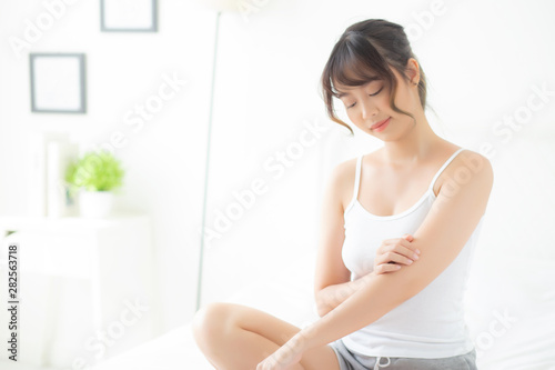 Beautiful portrait young asian woman smile applying sunscreen cream or lotion on skin care at bedroom, beauty asia girl using makeup and cosmetic for smooth and silky, wellness and health concept. © N_studio