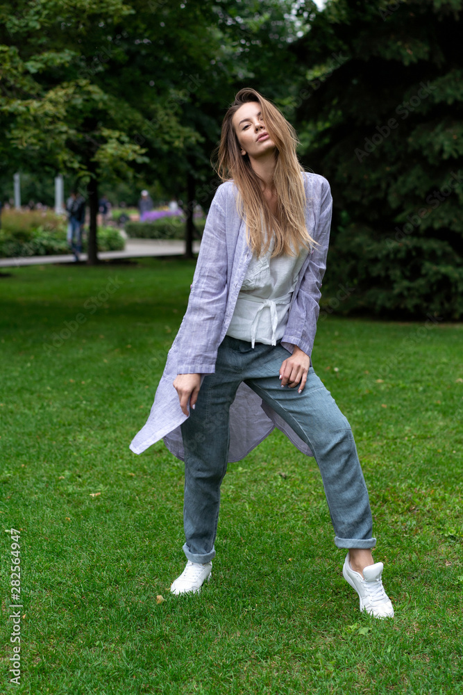 Young beautiful European girl, natural long hair. blue pants, white shirt, lilac jacket, barefoot posing, actively walking in park on grass. Linen womens clothing. Lifestyle, nature. Young beautiful European girl, natural long hair. blue pants, white shirt, lilac jacket, barefoot posing, actively walking in park on grass. Linen womens clothing. Lifestyle, nature.