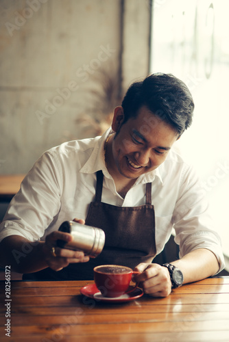 Asian barista sprinkles chocolate powder on drink in red cup.