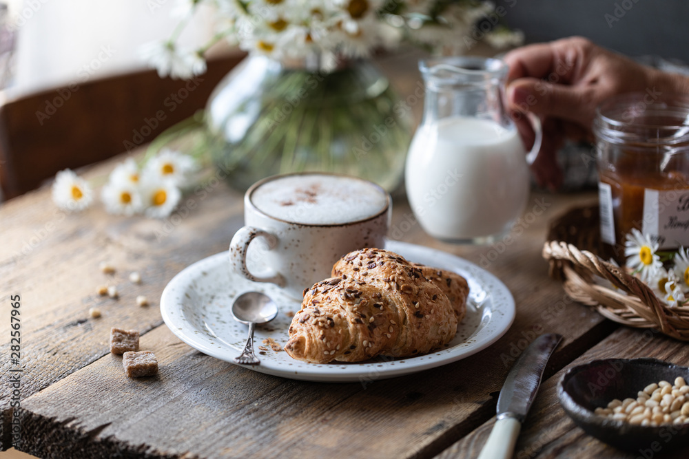 Breakfast cup of coffee and croissant with milk and peach or apricot jam on a wooden table. Bouquet of daisies. rustic Breakfast cup of coffee and croissant with milk and peach or apricot jam on a wooden table. Bouquet of daisies. rustic