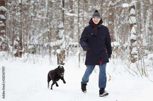 Man fun with his black labrador retriever in winter forest.