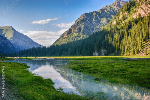 Idyllic summer landscape with hiking trail in the mountains with beautiful fresh green mountain pastures, river with reflection and forest. Terskey Alatoo mountains, Tian-Shan, Karakol, Kyrgyzstan photo