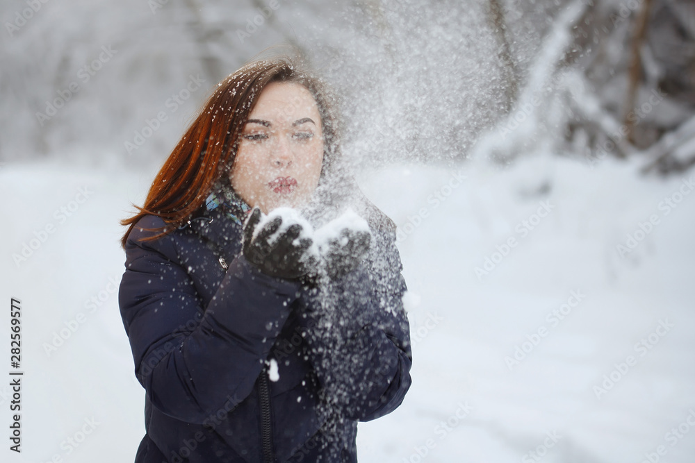 Young, pretty woman in a blue scarf and jacket in a snowy forest.