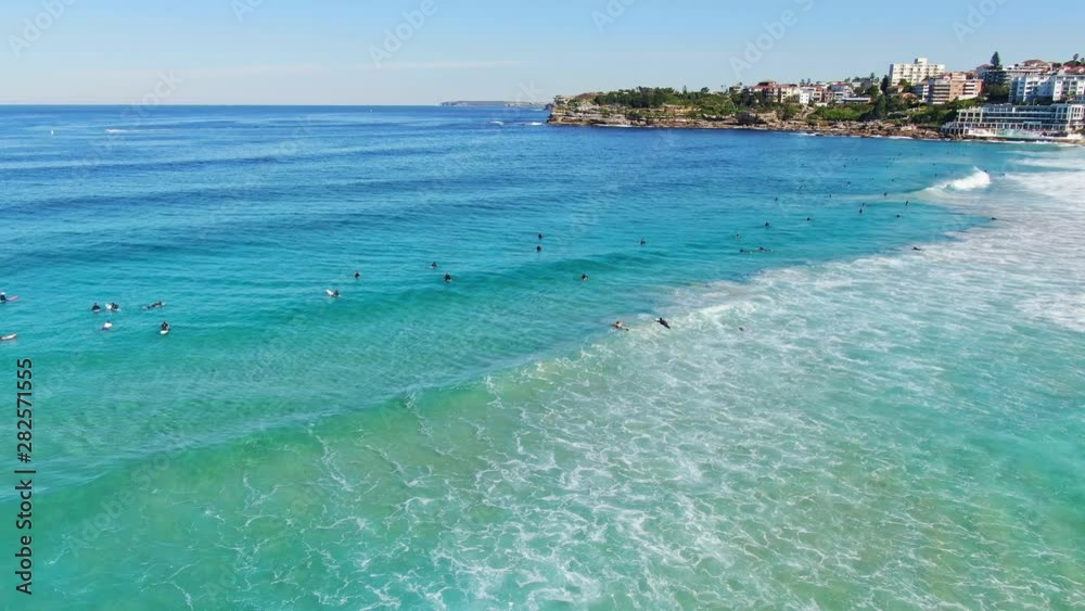 Dynamic 4k aerial drone panning flight over surfers in wetsuits waiting for good waves at world famous Bondi Beach, Sydney, New South Wales, Australia. Bondi Beach is a famous tourist destination. Dynamic 4k aerial drone panning flight over surfers in wetsuits waiting for good waves at world famous Bondi Beach, Sydney, New South Wales, Australia. Bondi Beach is a famous tourist destination.