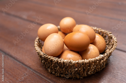 Close up of organic raw chicken eggs in basket on brown wooden floor background