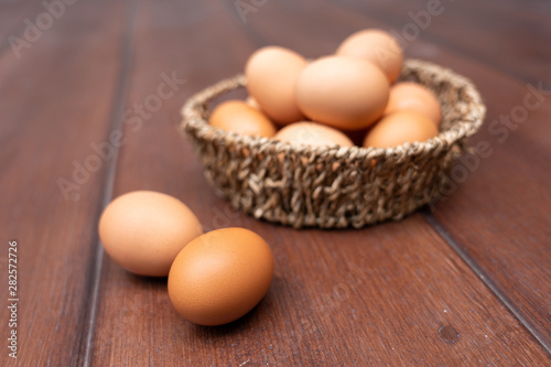 Close up of organic raw chicken eggs in basket on brown wooden floor background